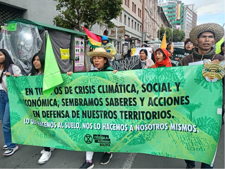 A photograph of a group of people in a protest march on a city street carrying various flags and signs.
