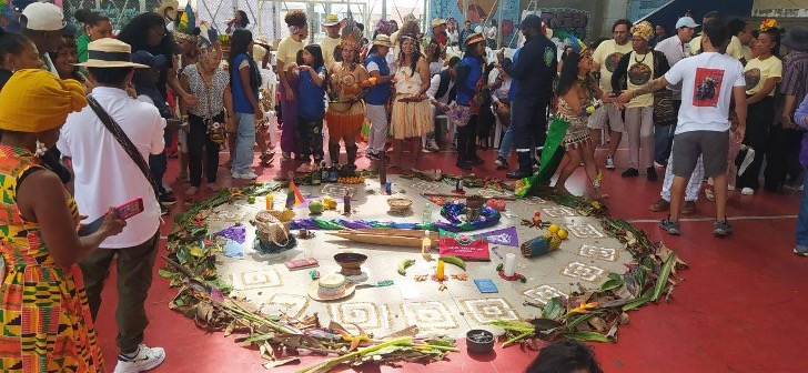 लाल फर्श वाले एक बड़े कमरे में खड़े लोगों के समूह की एक तस्वीर। फर्श पर एकबड़ा, गोलाकार क्षेत्र है।