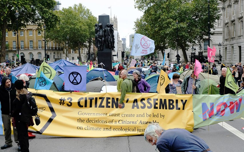 sprotestors hold up an XR sign reading "#3 Citizens' Assembly"treet