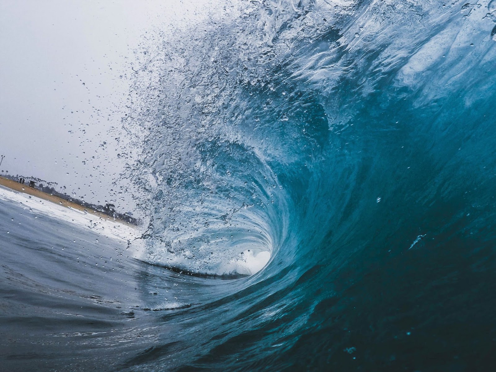 A
wave in Newport Beach, USA एक क्रिस्टल नीली लहर का बैरल किनारे की ओर गिर रहा है, जिसकी शिखा पानीछिड़क रही है।